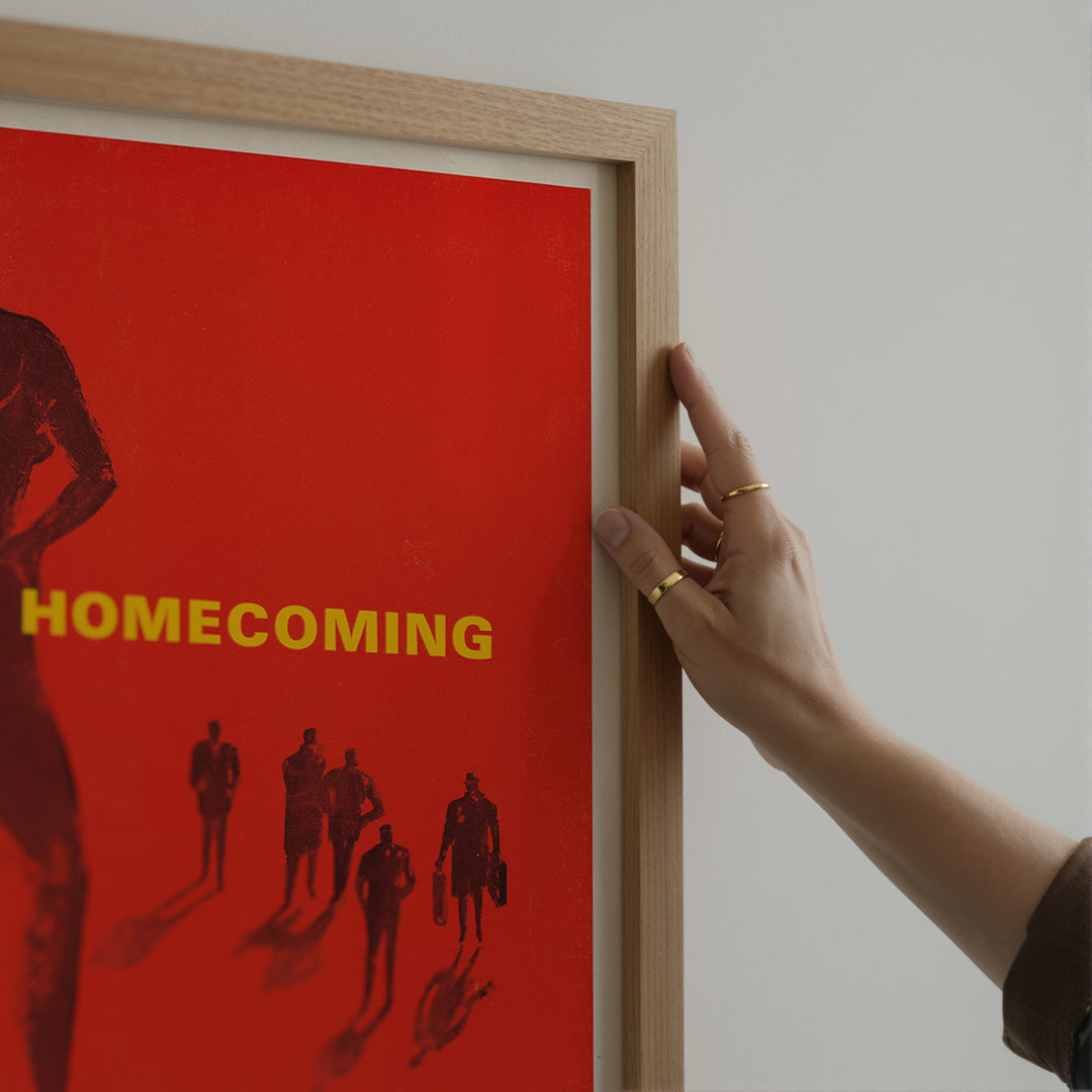 The Homecoming Poster featuring minimalist vintage style with red background, yellow text, and silhouetted black figures in a framed poster